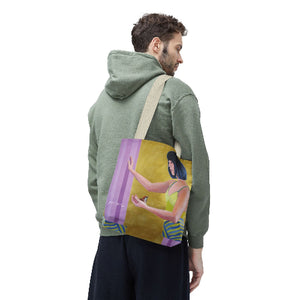 a tote bag with a po-art female portrait by kiki spring. The woman has black hair and the background is golden. The man carrying the back can be in his 30ties wearing a green hoodie. 