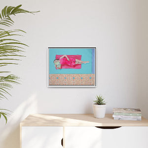 Framed artwork on a wall above a desk with a plant and books.