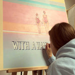 Load image into Gallery viewer, Person painting a colorful scene of two people on a beach with text.
