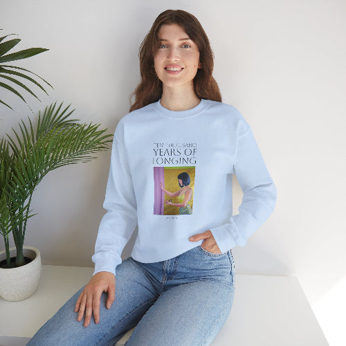 Person wearing a light blue sweatshirt with a graphic design, sitting on a white surface with a plant in the background.