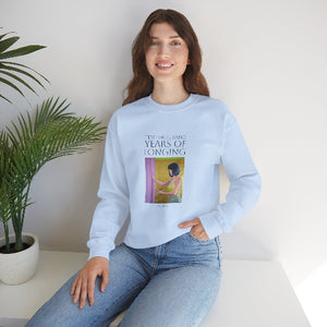 Person wearing a light blue sweatshirt with a graphic design, sitting on a white surface with a plant in the background.