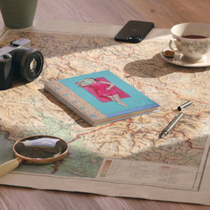 Notebook with a colorful cover on a map with a camera, phone, tea cup, and pen nearby.